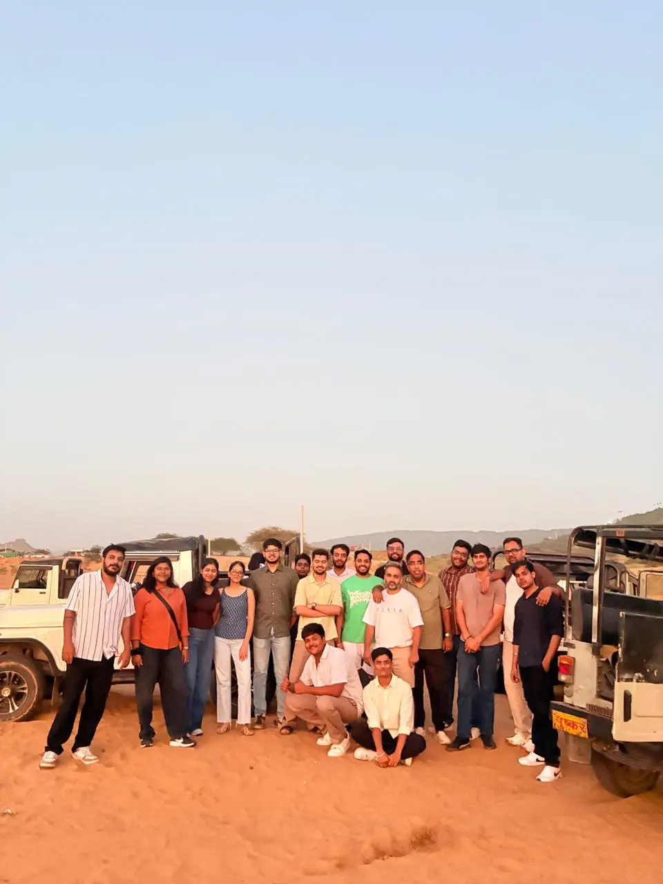 A travel group standing on desert sand beside safari jeeps at dusk