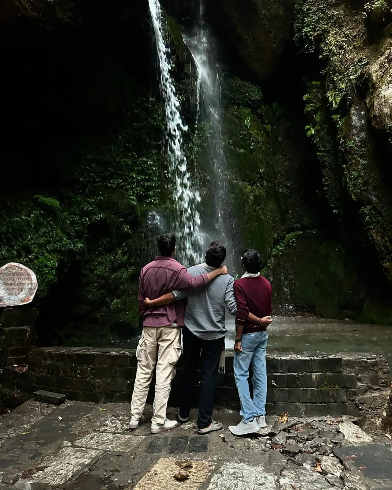 Three friends looking up at a waterfall in a mossy gorge